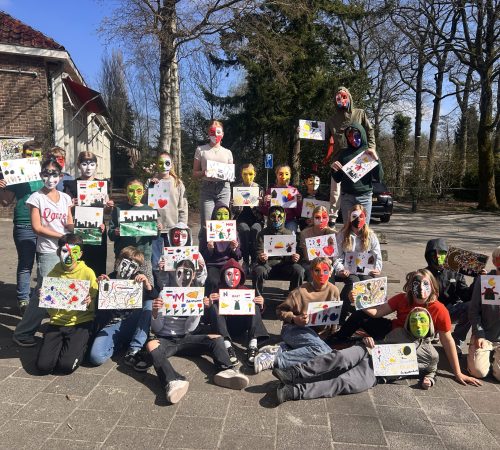 Leerlingen met zelfgemaakte maskers tonen trots hun tekeningen tijdens een kunstproject op het schoolplein.